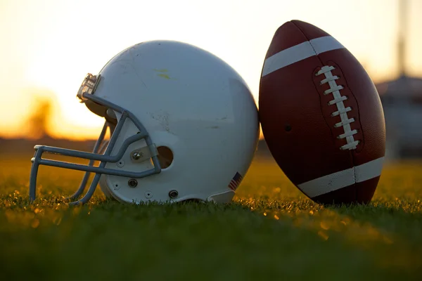 Футбол и шлем на поле на закате Стоковая Картинка