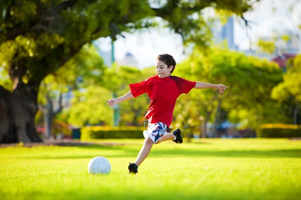 Молодой взволнованный мальчик, пинающий шар в траву Стоковое Изображение