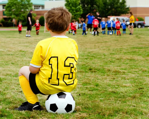 Молодой мальчик в единообразных смотреть организованной молодежи футбол или футбол игра от боковые Лицензионные Стоковые Изображения